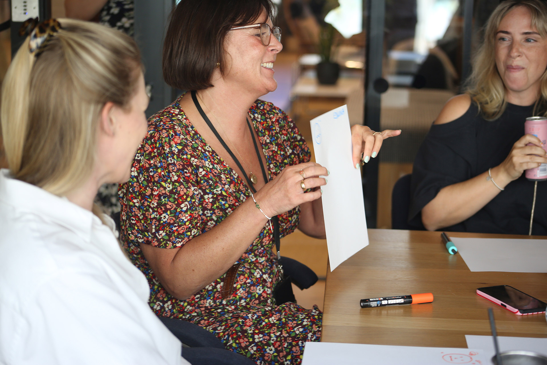 A woman holding up a piece of paper showing her doodle to other people. She is smiling.